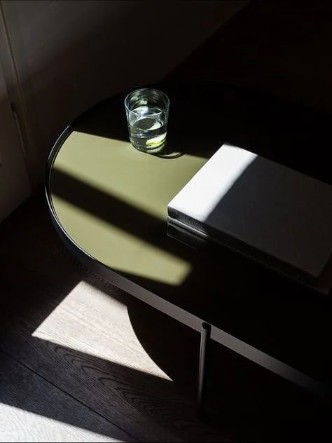 Een donkergekleurde tafel met een glas water en een boek belicht door zonlicht.