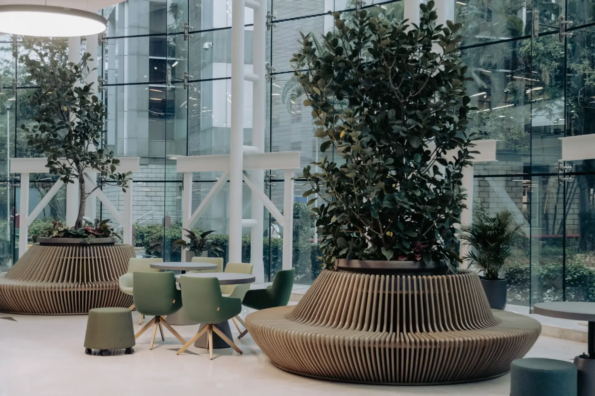 Moderne kantoorhal met grote planten in houten plantenbakken, groene stoelen en glazen wanden.